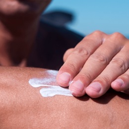 Image of someone applying sunscreen to their arm on the beach. 